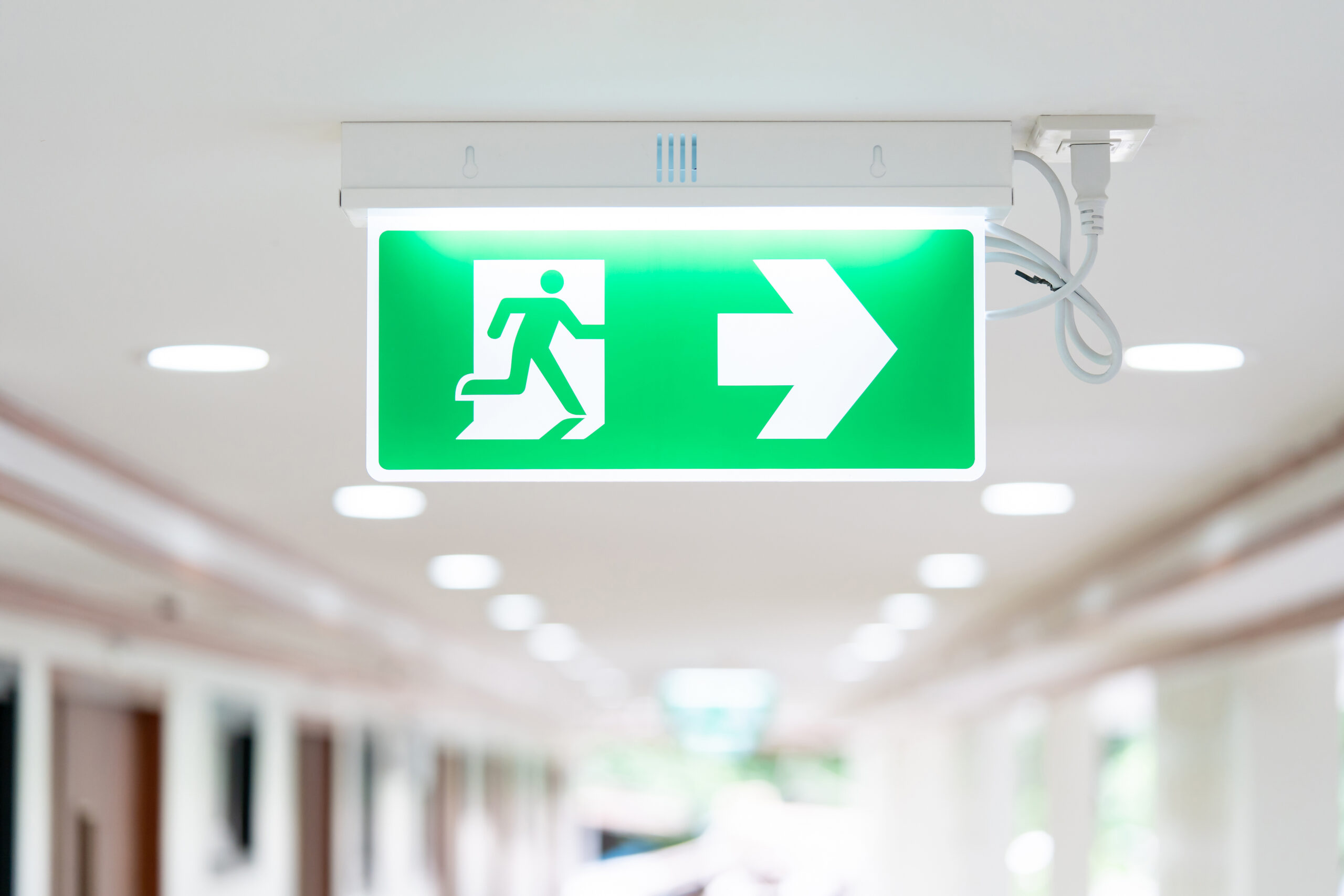 A arrow light box sign of emergency fire exit is hung on the ceiling in hospital walkway, idea for event fire or evacuation drills.